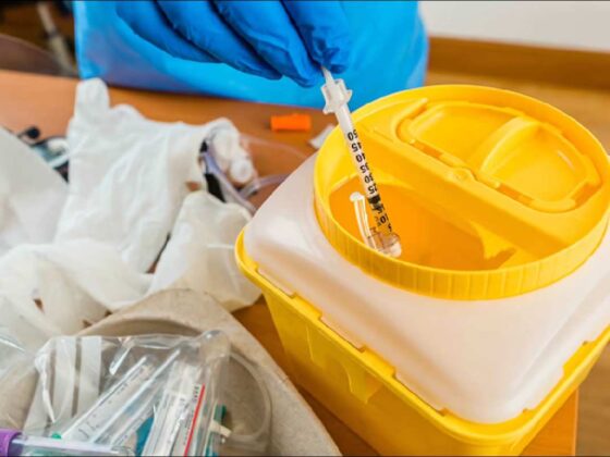 Used syringe being safely disposed of in a yellow sharps container with medical gloves and supplies nearby
